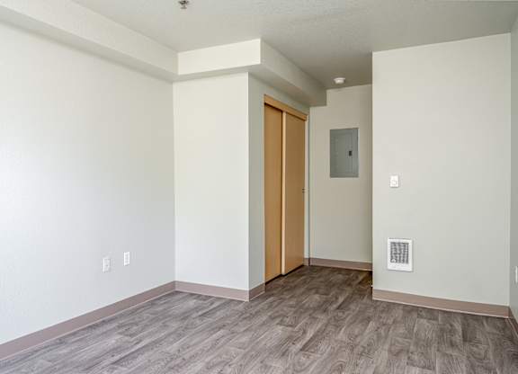 A room with a wooden floor and a white wall with a switchboard and a door.