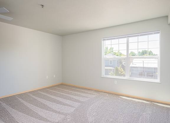 A room with a carpeted floor and a window showing a view of a house.