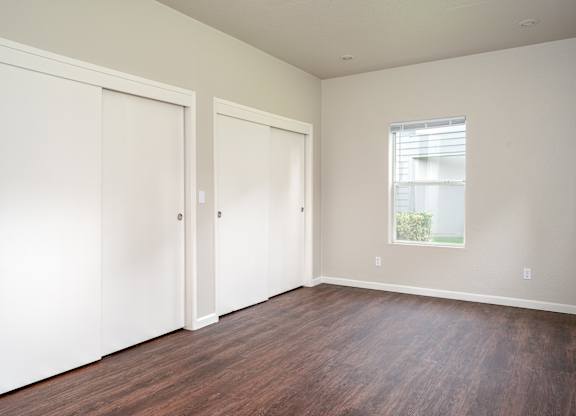 A bedroom with two closet doors and a window.