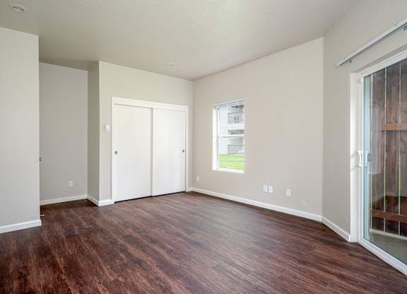 A bedroom with wood flooring, double closet doors and double patio doors.