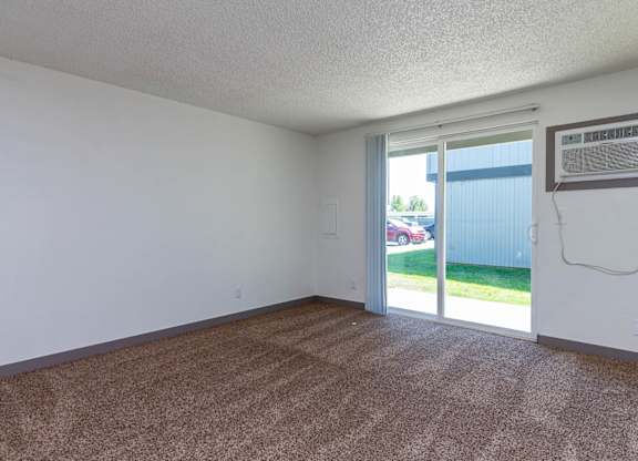 A room with a carpeted floor and a sliding glass door leading to a backyard.