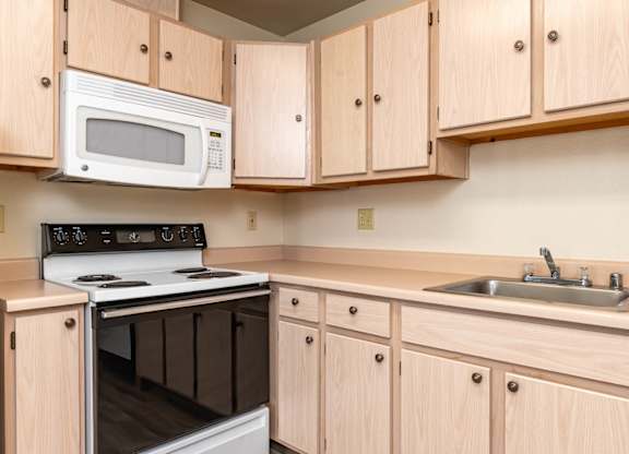 A kitchen with a white microwave oven mounted above a stove and wooden cabinets below.