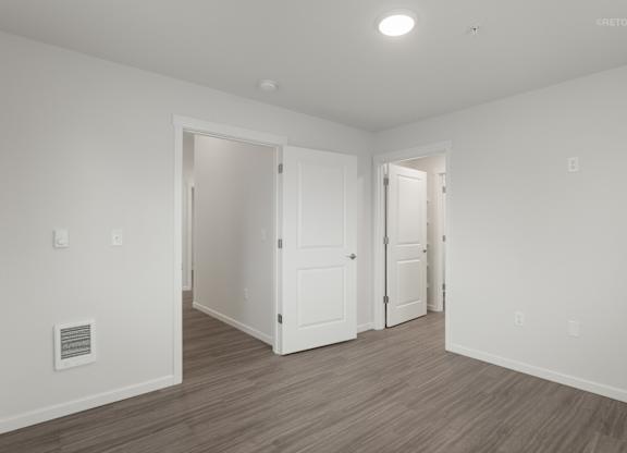 A room with white walls and wooden flooring with two doors.