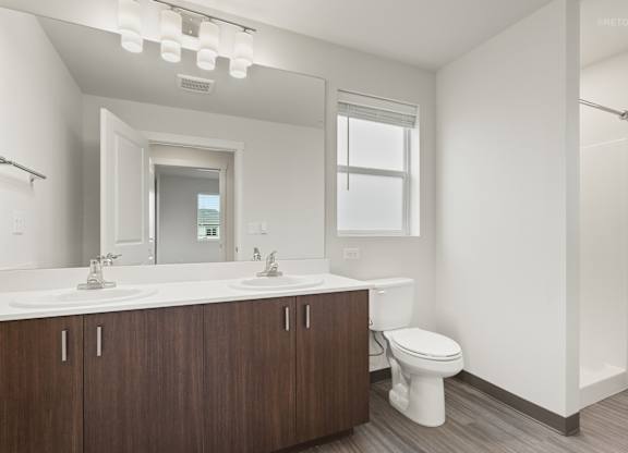 A white bathroom with a wooden vanity and a white toilet.