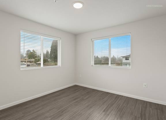 A room with wooden flooring and two windows with blinds.