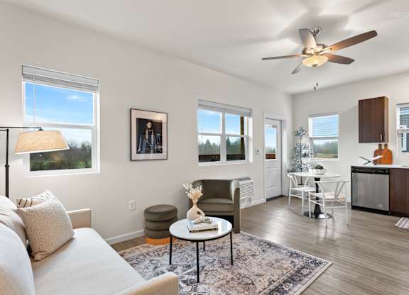 A living room with a couch, a table, a fan, and a window.