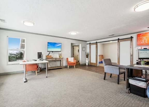 A room with a desk, chairs, and a TV on the wall.