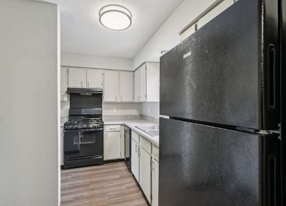A black refrigerator is in the foreground of a kitchen.