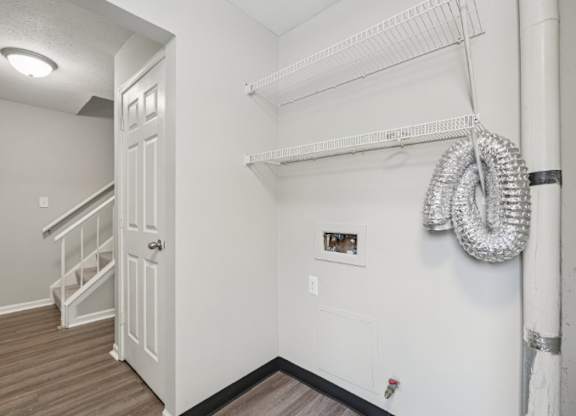 A white door is on the left side of a room with a white wall and a white shelf.