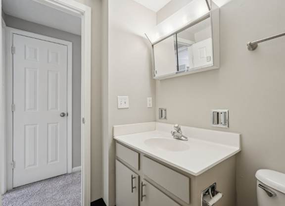 A white bathroom with a sink, mirror, and toilet.