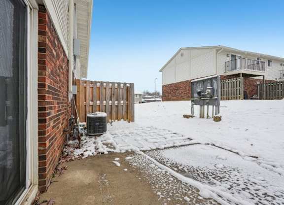 A snow-covered ground with a building and a fence in the background.