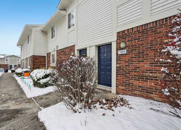 A snow-covered ground with a building and a bush in front.