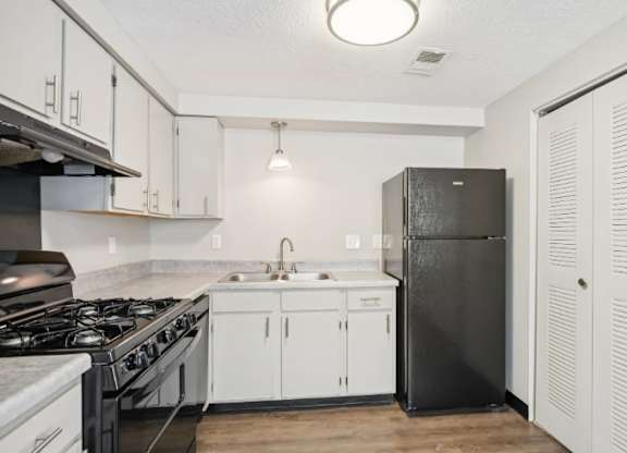 A kitchen with a black refrigerator and white cabinets.