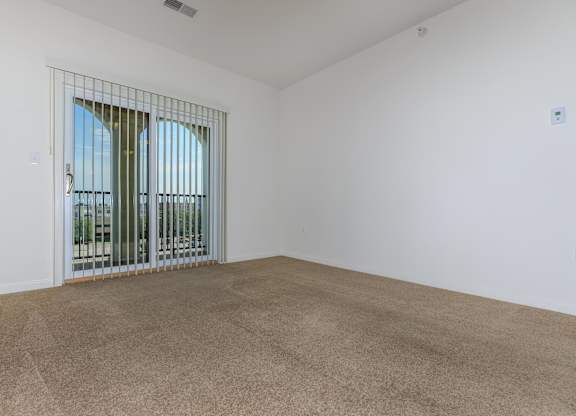 A room with a carpeted floor and a window with a metal grill.