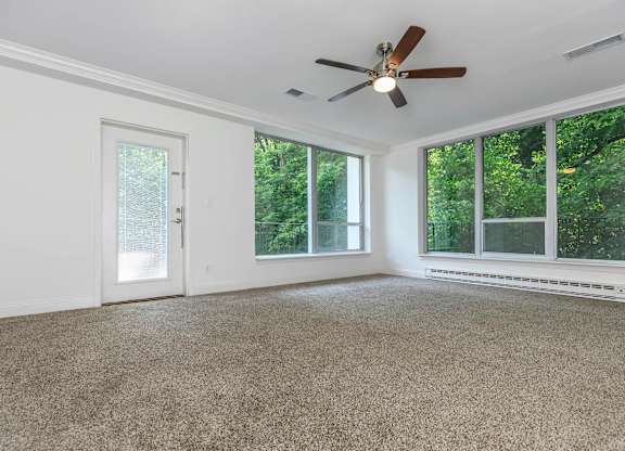 A room with a ceiling fan and large windows.