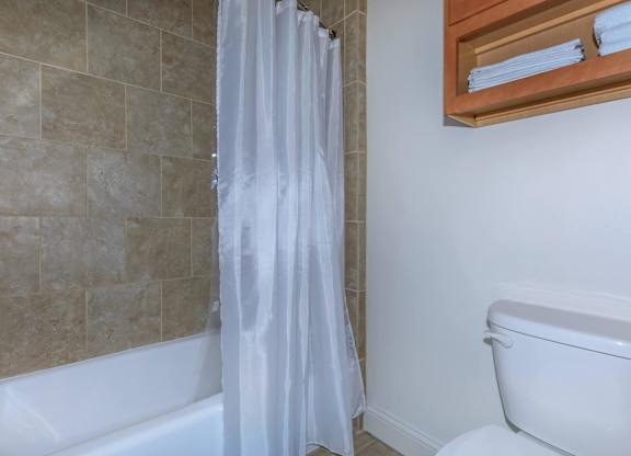 A white shower curtain in a bathroom with a white tub.