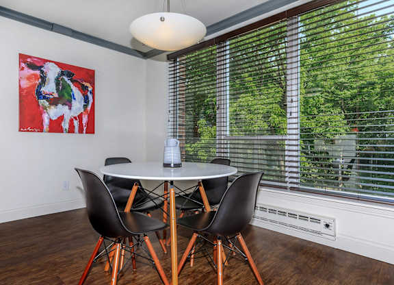 A dining room with a table and chairs and a painting on the wall.