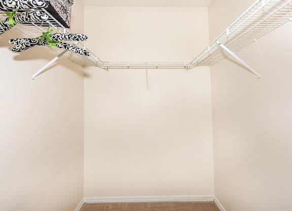 A white closet with a hanging shelf and clothes.