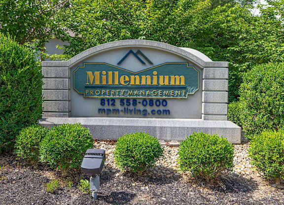 A sign for Millennium Property Management is displayed in front of some bushes.