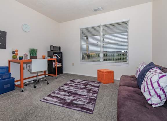 A living room with a purple couch and a white clock on the wall.