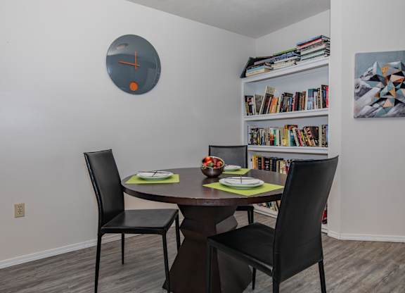 A dining room with a round clock on the wall and a bookshelf with books.