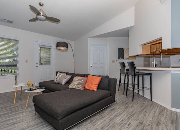 A living room with a grey couch and a fan on the ceiling.