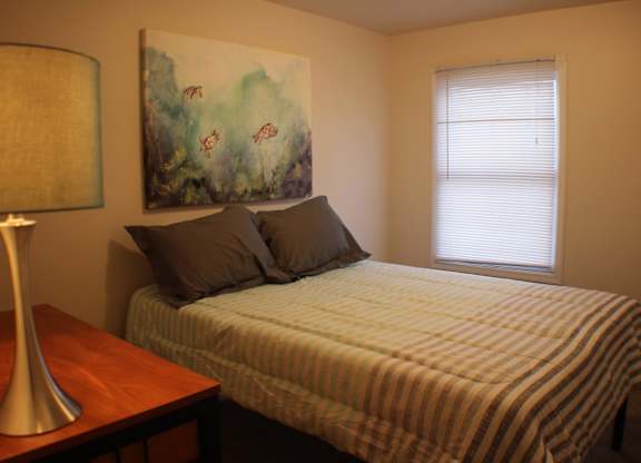 A bedroom with a bed, a lamp, and a painting on the wall.