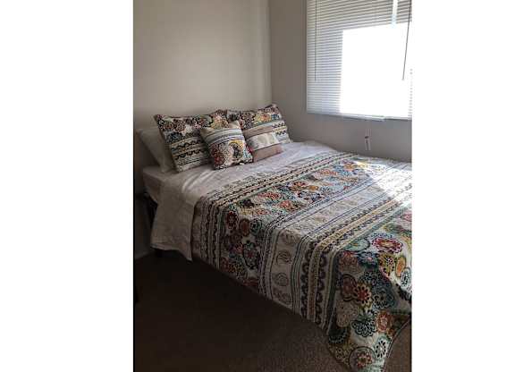 A bed with a white comforter and a multicolored blanket on it.