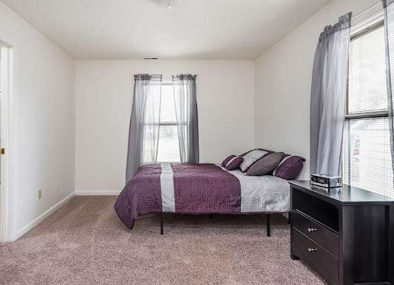 A bedroom with a bed, nightstand, and window.