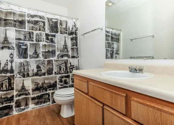 A bathroom with a toilet, sink, and a shower curtain with black and white photos on it.