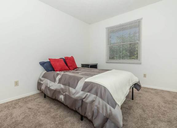 A bedroom with a bed covered in a grey and white comforter and two pillows, one red and one blue.