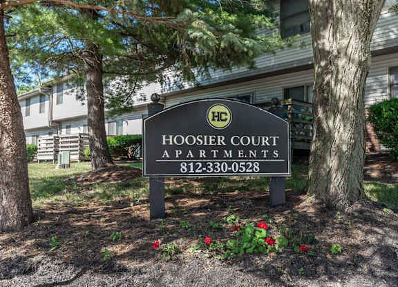 A sign for Hoosier Court Apartments is in front of a tree and a building.