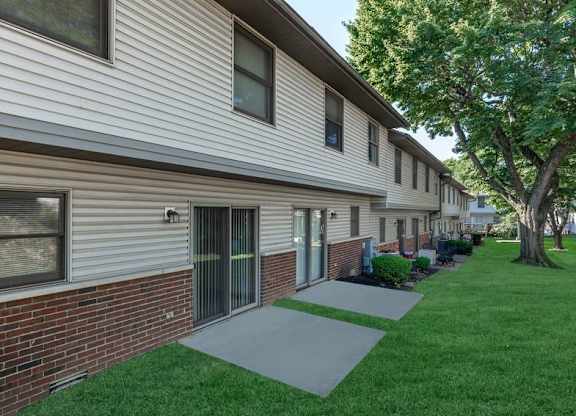 A building with a grey siding and a brick base with a green lawn in front.