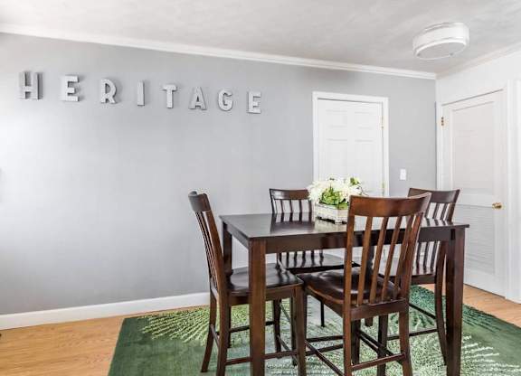 A dining room with a table and chairs and a green rug.
