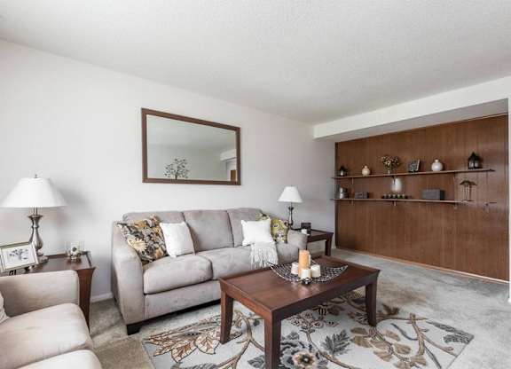 A living room with a grey couch, a wooden coffee table, and a mirror on the wall.