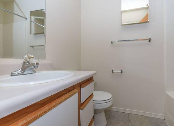 A white toilet sits in a bathroom next to a sink and a bathtub.