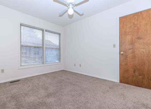 A room with a ceiling fan, carpeted floor, and a wooden door.