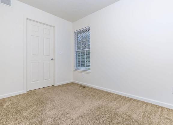 A room with a carpeted floor, a door, and a window with blinds.