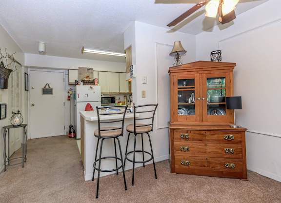 A kitchen with a white refrigerator, a wooden cabinet, and a bar stool.