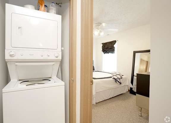 A white oven and dryer are in a small room with a bed in the background.