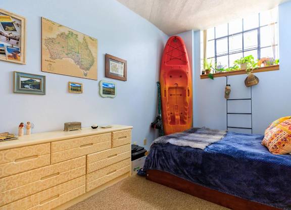 A room with a bed, dresser, and a surfboard.