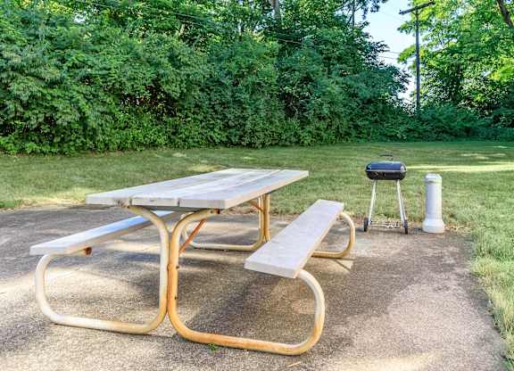 A picnic table with a grill and a cooler on a concrete surface.