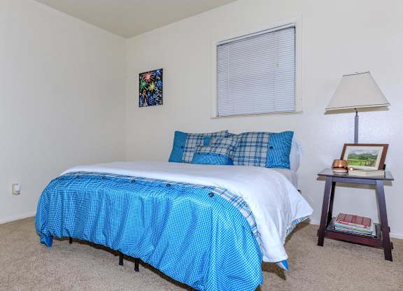A bed with a blue and white comforter is in a room with a lamp and picture frame on a side table.