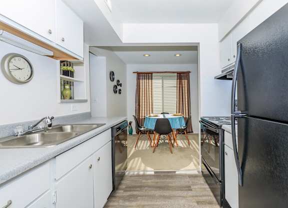 A kitchen with a black refrigerator and a dining table with chairs.