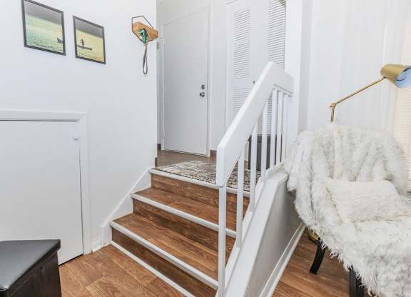 A white chair with a fluffy white blanket is in front of a staircase.