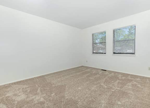 A room with a carpeted floor and two windows.
