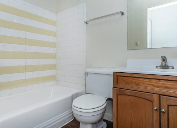 A white toilet sits next to a white bathtub in a bathroom with yellow and white tiles.