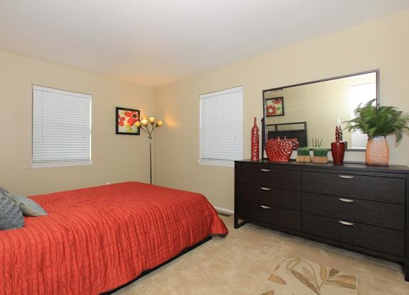 A bedroom with a red bedspread and a black dresser.