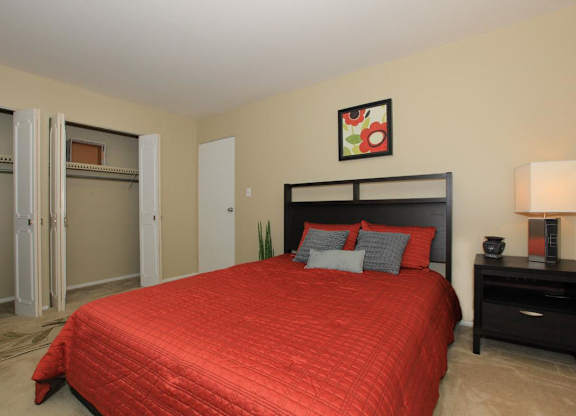 A bedroom with a red bedspread and a black headboard.