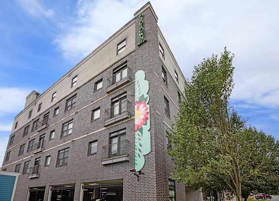 A tall building with a green sign on the top and a large flower mural on the side.